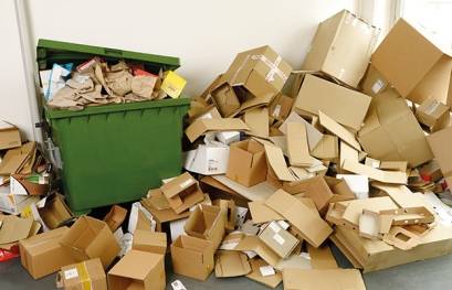 Rollbare Altpapiertonne mit einem Berg an Altkartons daneben