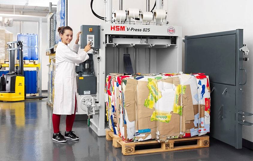 Angestellte neben Vertikalballenpresse HSM V-Press 825 mit geöffneter Tür und ausgeworfenem Ballen